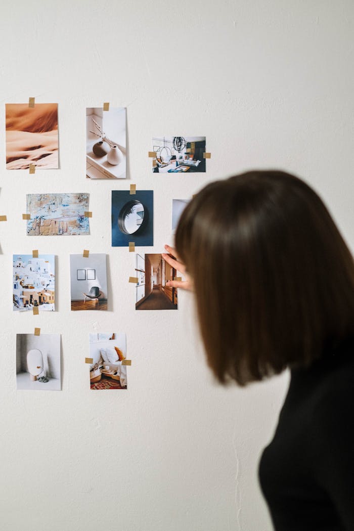A woman arranges various art photographs on a light wall, creating a minimalistic display.
